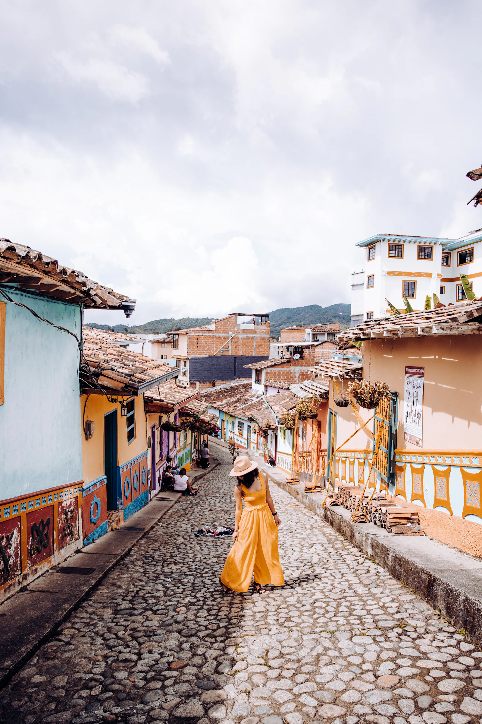 International travelers walking through a sunlit Colombian town with lush green landscape and colonial architecture in the background